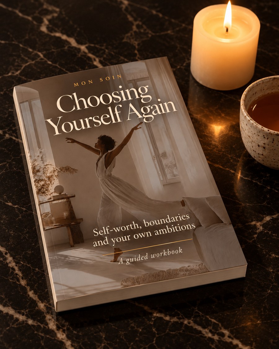 A candle and her Choosing Yourself Again book on a dark marble table